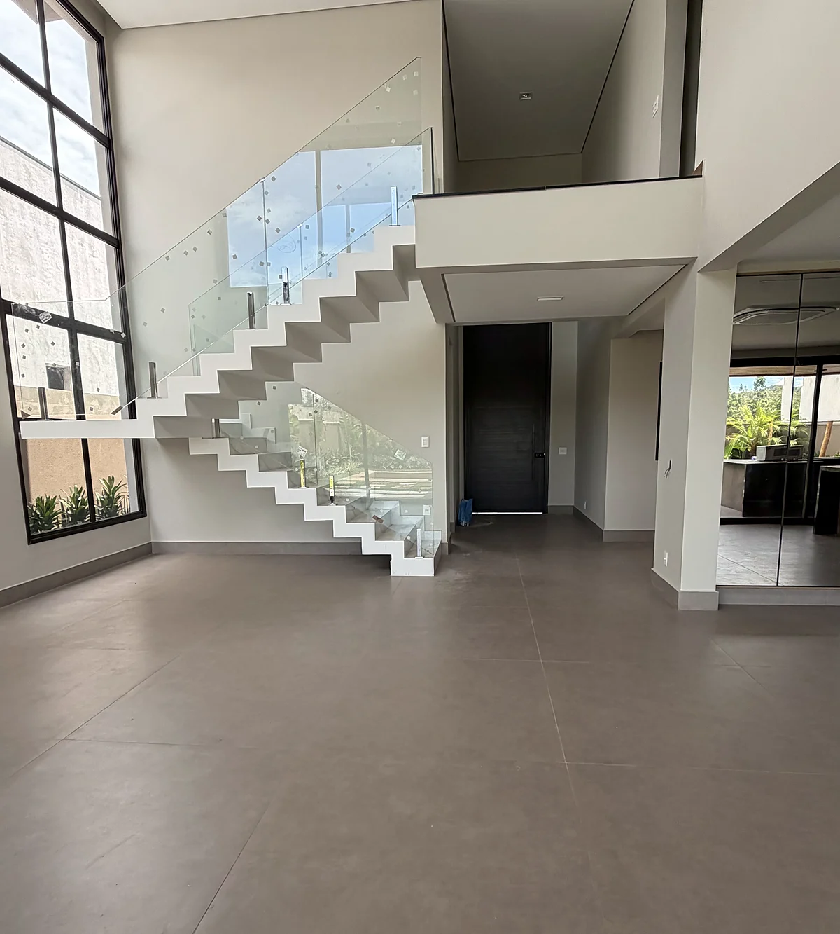 Sala de pé-direito duplo com escada de vidro, obra executada pela HSM Engenharia