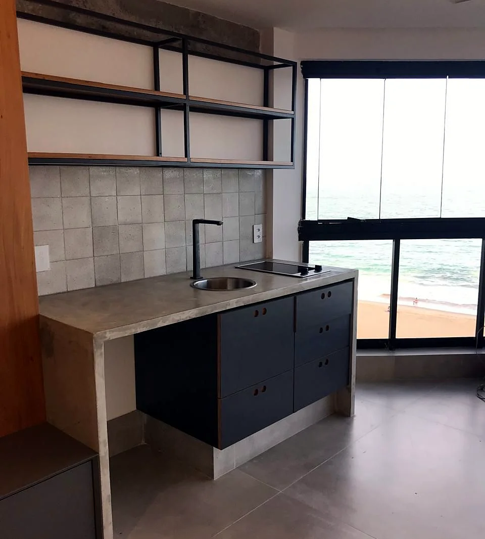 Cozinha integrada de apartamento com armários escuros, prateleiras abertas e vista pela janela